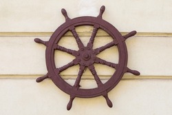 An old steering wheel from a ship on the wall of a house, an element of naval architecture.