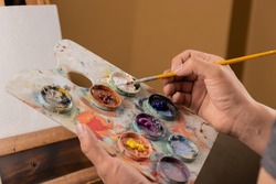 paint stained hand holding a brush, artist mixing colors on a palette, work tools, hobbie, creative lifestyle in studio, colorful water paint texture