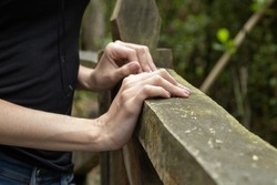 details of the hands of a person resting on a rustic wooden handrail, knuckles, wrist and fingers, skin texture, wallpaper