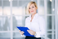 Beautiful blonde business woman in a white shirt with a folder of documents in an office building.