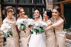 Group portrait of the bride and bridesmaids. A bride in a wedding dress and bridesmaids in golden dresses hold stylish bouquets of flowers on their wedding day.