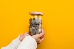 Hands and coins in a savings jar money saving on yellow background money saving concept Plant a plan to save money for children.