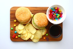 Hamburger, fried potato, candy, coke on wooden plate