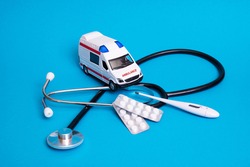 Toy ambulance car and stethoscope on blue background close up