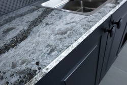Quartz counter worktop with beautiful pattern and stainless steel sink on black wooden kitchen.