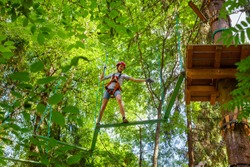 Teenager boy wearing safety harness passing Z-shaped balance beam obstacle at a ropes course in outdoor treetop adventure park
