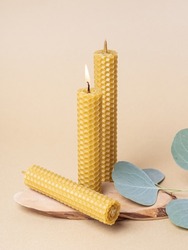 Three handmade beeswax candles on beige background. Handmade eco product. Honey aroma. Lighted candle. Easter concept
