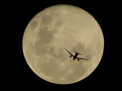 jet plane flying over the full moon that has a golden hue during a clear and dark night, Brazil