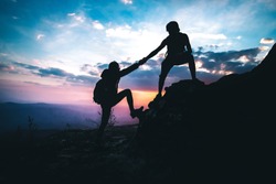 A man helping a woman to up on the mountain in hiking activity. teamwork concept. silhouette style