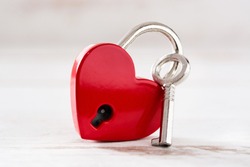 Red padlock hearts with key on white wooden background. 