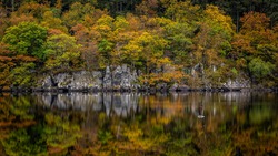 A small iron cross in the Trossachs National park reflecting in the calm autumnal waters of Loch Ard