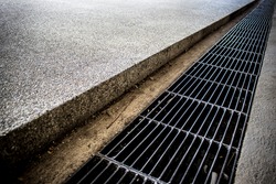 Iron grate of water drain or waterway parallel the concrete walkway