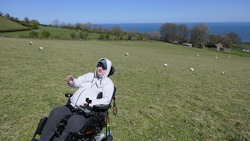 Man in a wheelchair sitting in a field with sheep on a farm