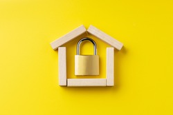 house symbol made by wooden blocks over yellow background with padlock inside. outer space. home protection and security concept.