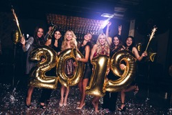 Happy new year! Beautiful young women in evening gown holding balloons and looking at camera with smile while celebrating in nightclub
