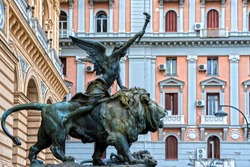 An old, bronze statue of a winged goddess sitting on a lion in the center of Naples, Italy.