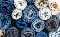 background from stack of different rolled jeans. Roll blue denim jeans arranged in stack. Jeans pyramid. Recycling old blue jeans on wooden table. Denim upcycle. Zero waste