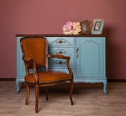 Retro brown leather armchair near blue dresser, tender bouquet and two frames. Blue and brown vintage interior. Brown room with ethnic dresser and chair. Antique cupboard. Clothes closet. Vanity Table