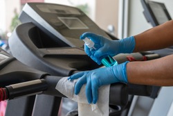 Staff using wet wipe and alcohol sanitizer spray to clean treadmill in gym. Antiseptic,disinfection ,cleanliness and heathcare , anti virus concept. Anti Corona virus (COVID19).Selective focus.