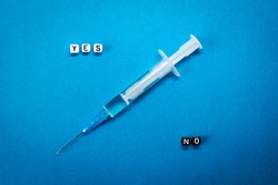 Yes No words made of square letters and a syringe on blue background. Pros and cons of coronavirus vaccine, concerns and doubts about COVID-19 vaccination concept