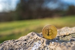 Close-up of Bitcoin on a stone outdoor with green natural background with copy space. Single physical metal gold shining BTC cryptocurrency coin. Environment impact of crypto mining concept