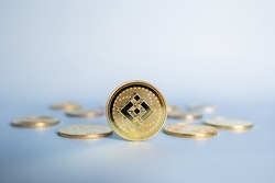 Binance BNB cryptocurrency coin standing centrally placed among bunch of crypto gold coins on blue background. Close-up, soft focus.