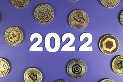 Cryptocurrency in 2022 price prediction, value forecast concept. Golden crypto coins Bitcoin, Uniswap, Nano, Tezos, Ankr, Chainlink next to the white year numbers on purple background.