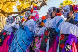 Group of unrecognizable women wearing traditional sugar skull masks and costumes for Dia de los Muertos celebration