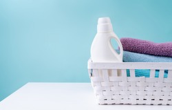 Laundry concept. Laundry basket with a detergent bottle and a pile of clean towels on white table isolated on blue background with copy space