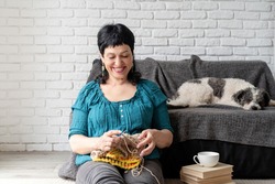 Stay home. Smiling middle aged woman sitting at home knitting. Copy space