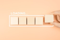 Loading bar with wood cube on pastel background. Wooden blocks with the word LOADING in loading bar progress. Concept loading. Hand putting wooden cube block shape on load