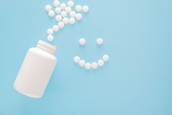 smiling face lined with pills. White jar and scattered white pills. Smiling face made from white round pills on blue background. Medicine and health care concept. Top view. copy space