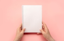 Notepad mockup. female hands holding blank spiral notepad or calendar over pink table background. hands shows open notebook. Female hands holding blank white notebook. copy space