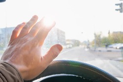 the driver's hand and fingers at the wheel of a moving car cover the sun, which blinds the eyes and does not see the roadway