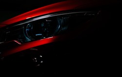 Closeup headlight of shiny red luxury SUV compact car. Elegant electric car technology and business concept. Hybrid auto and automotive concept. Car parked in showroom or motor show. Car dealership.