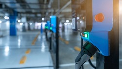 Blur photo of electric car charging station for charge EV battery. Plug for vehicle with electric engine. EV charger. Clean energy. Charging point at car parking lot. Future transport technology.