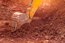 Backhoe working by digging soil at construction site. Bucket of backhoe digging soil. Crawler excavator digging on dirt. Closeup backhoe bucket of yellow backhoe. Earthmoving. Trenching machine.