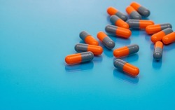Orange-gray antibiotic capsule pills on blue background. Antibiotic drug resistance. Pharmaceutical industry. Prescription drug. Capsule pills production manufacturing. Pharmacology and toxicology.