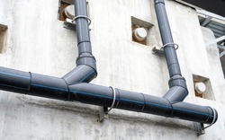 Polyethylene pipes drain water from sky train tracks. HDPE pipeline drainage. Black PE tube was installed on a building wall. Polyethylene pipe network. Pipe construction. Water drainage HDPE pipe.