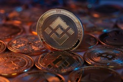 Binance BNB Cryptocurrency Physical Coin placed on crypto altcoins and lit with orange and blue lights. Macro shot. Selective focus.