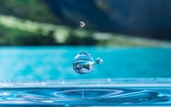 close up of a water drop impacting a body of water and reflecting the background