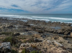 View sea shore with ocean waves, sharp rocks, stones and green vegetation at Rota Vicentina wild coast near Porto Covo, Portugal
