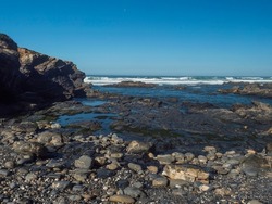View of wild Rota Vicentina coas with ocean waves and sharp rocks, stones and cliffs near Vila Nova de Milfontes, Portugal. Sunny day, blue sky.