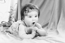 6 months old child with opened mouth lying on her front  with amazed face. Black and white photo