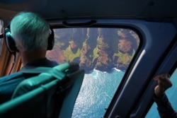 Old man looking through the window of a helicopter during a sightseeing flight over the dramatic ridges of the Na Pali coast on the northwestern side of Kauai island in Hawaii