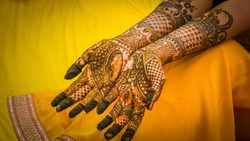 Henna painting, mehendi on bride's hands with the yellow dress background. Wedding preparation in India.