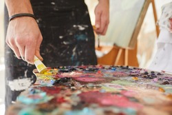 Close up background image of unrecognizable male artist putting paint on palette while painting pictures in art studio, copy space