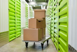 Background image of cart with cardboard boxes in empty hall of self storage facility, copy space