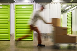 Blurred motion shot of unrecognizable man pushing cart with boxes while running in self storage facility, copy space