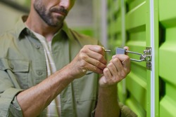 Close up of handsome man opening padlock on door of self storage unit , copy space